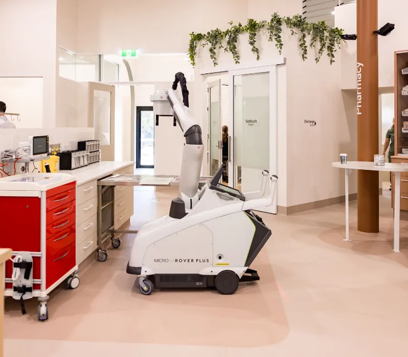 MICRO-X Rover Plus mobile X-ray unit positioned in a bright, modern clinical room with medical equipment and cabinetry in the background